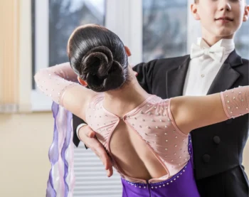Un couple de danseurs souriants, l'homme en chemise noire, la femme en robe violette et coiffure élégante.