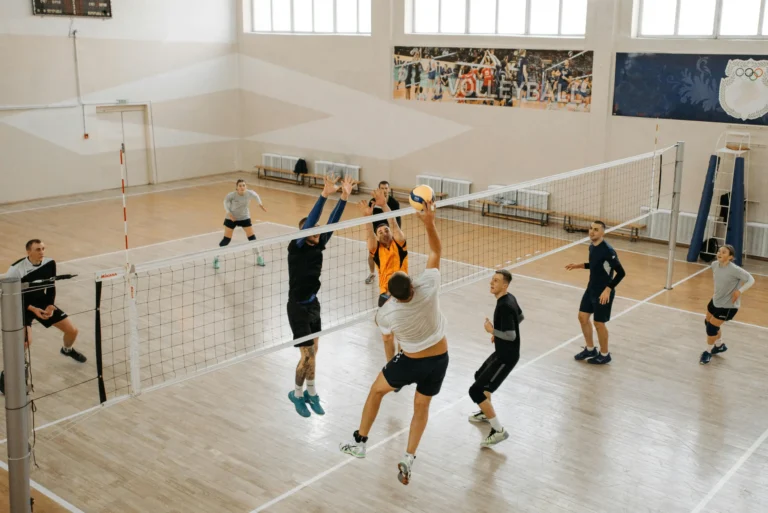 Les équipes de volley-ball jouent dans un gymnase ; les joueurs sautent et essaient de renvoyer la balle par-dessus le filet.