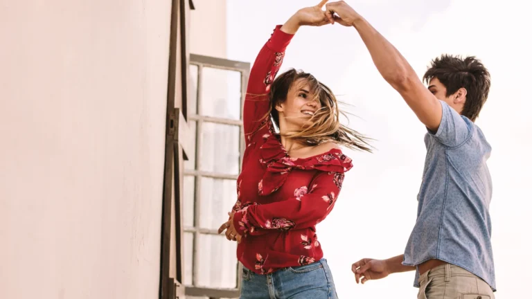 Kobieta w czerwonej kwiecistej bluzce i dżinsowych spodenkach tańcząca taniec towarzyski z mężczyzną w niebieskiej koszuli